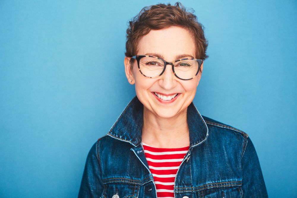 Headshot of a woman with short hair and glasses smiling in a striped shirt and denim jacket.