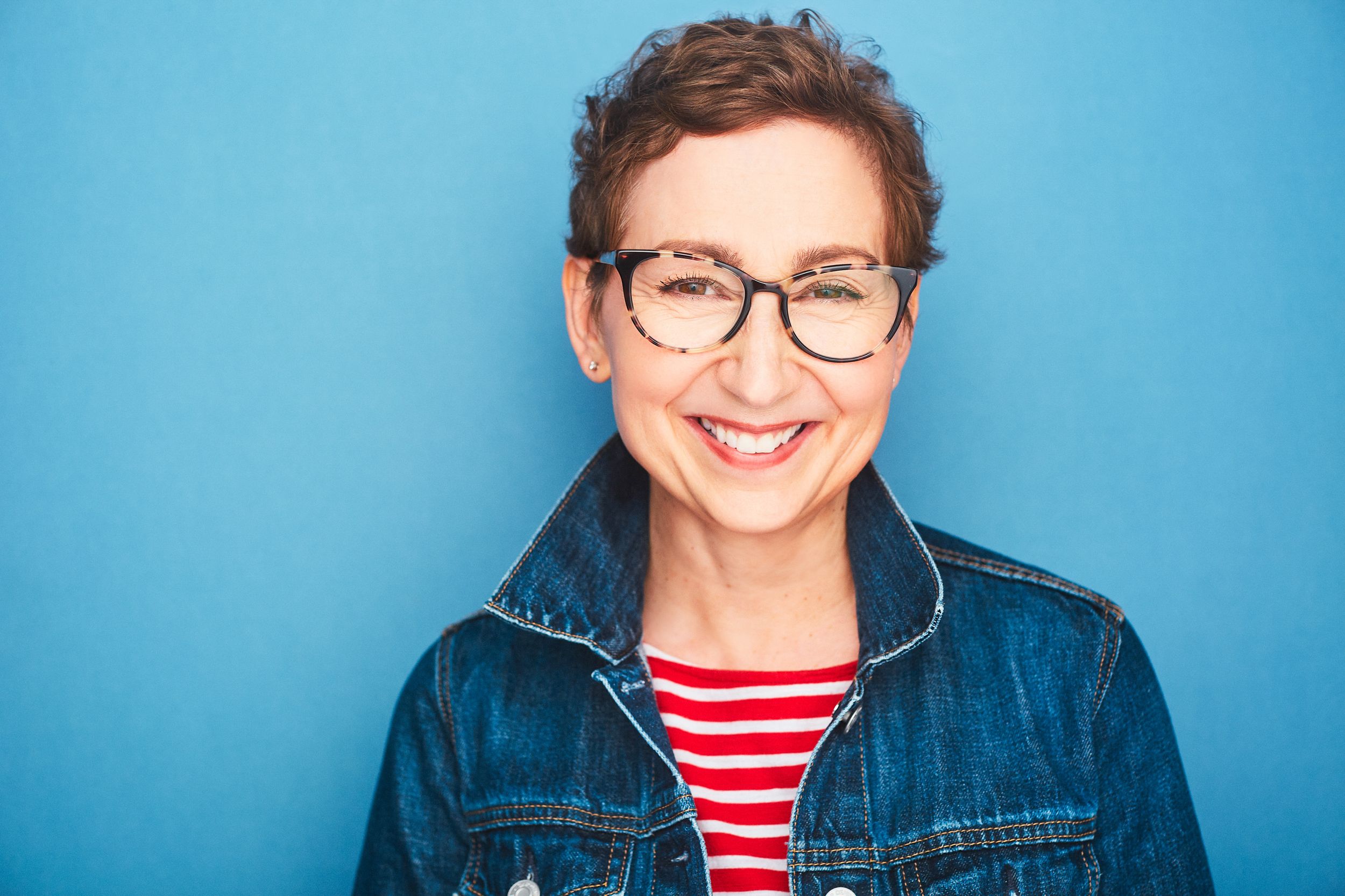 Headshot of a woman with short hair and glasses smiling in a striped shirt and denim jacket.