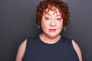 Headshot of a woman with short curly red hair in a grey shirt.