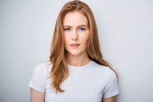 Headshot of a beautiful woman in a white t-shirt with hair falling over her shoulders.