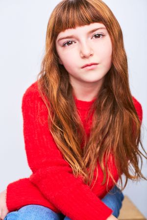Headshot of a young girl with long red hair and bangs in a bright red sweater.