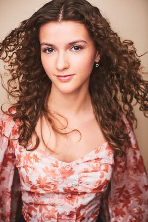Headshot of a beautiful teenage girl with long curly hair wearing a floral pink and white shirt and hair blowing in the wind.