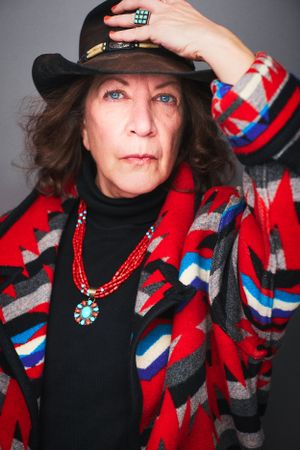 Headshot of a woman in a red patterned coat placing a cowboy hat on her head.