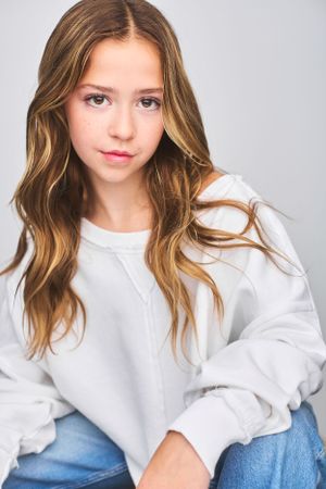 Headshot of beautiful young girl in an oversized white sweatshirt and jeans, sitting with wavy blonde hair falling over her shoulders.