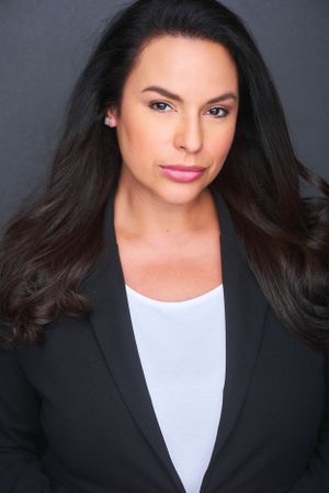 Professional headshot of a brunette woman in a blazer with long brown hair.
