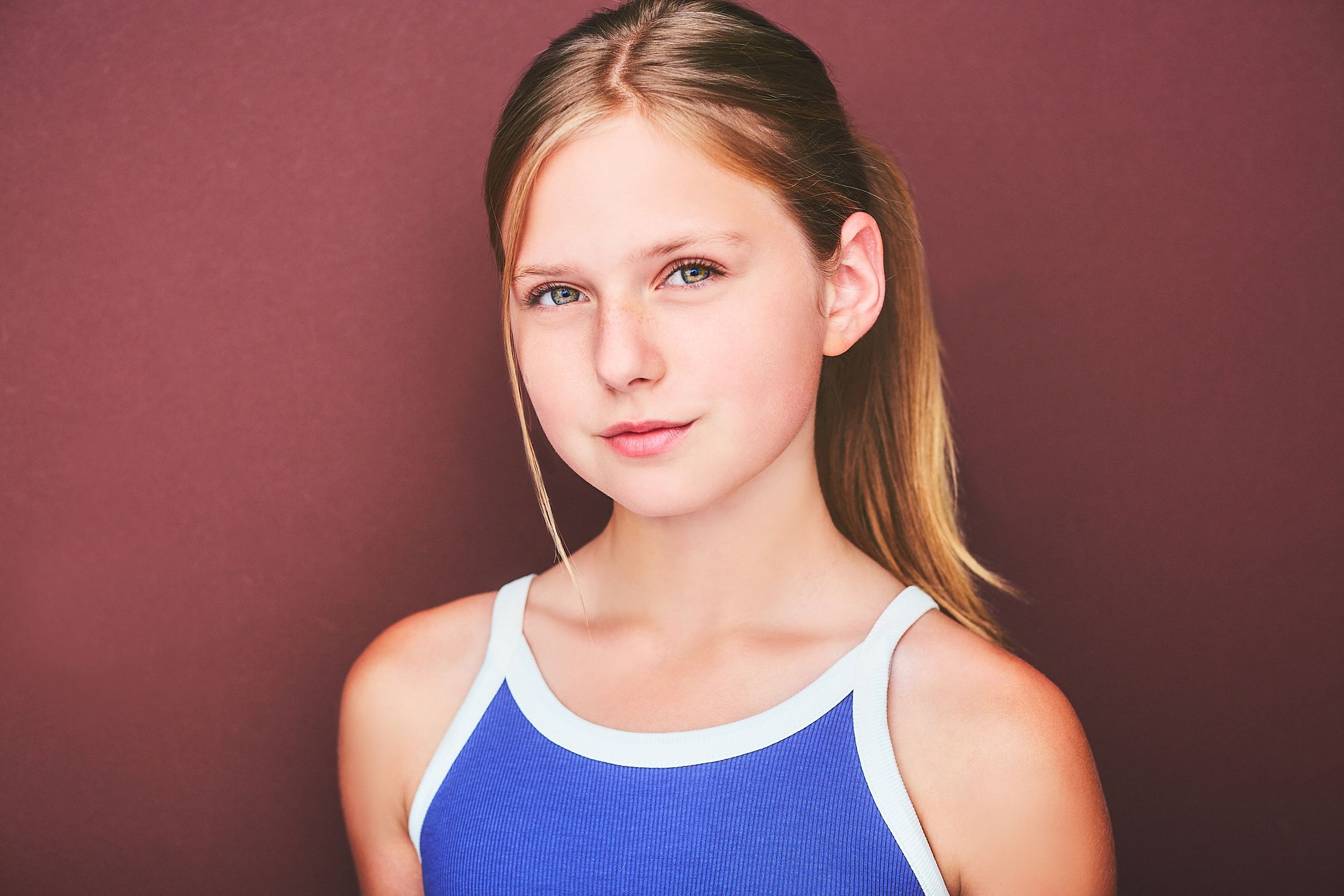 Headshot of a beautiful young girl in a pony tail and blue tank top.