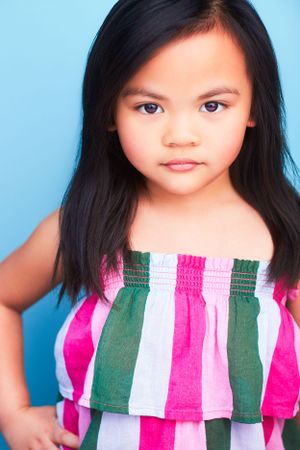 Adorable young girl in a striped stress looking straight at the camera with her hand on her hip.