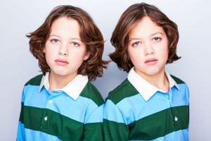 Portrait of two twin boys in striped lacrosse shirts back to back staring at the camera.