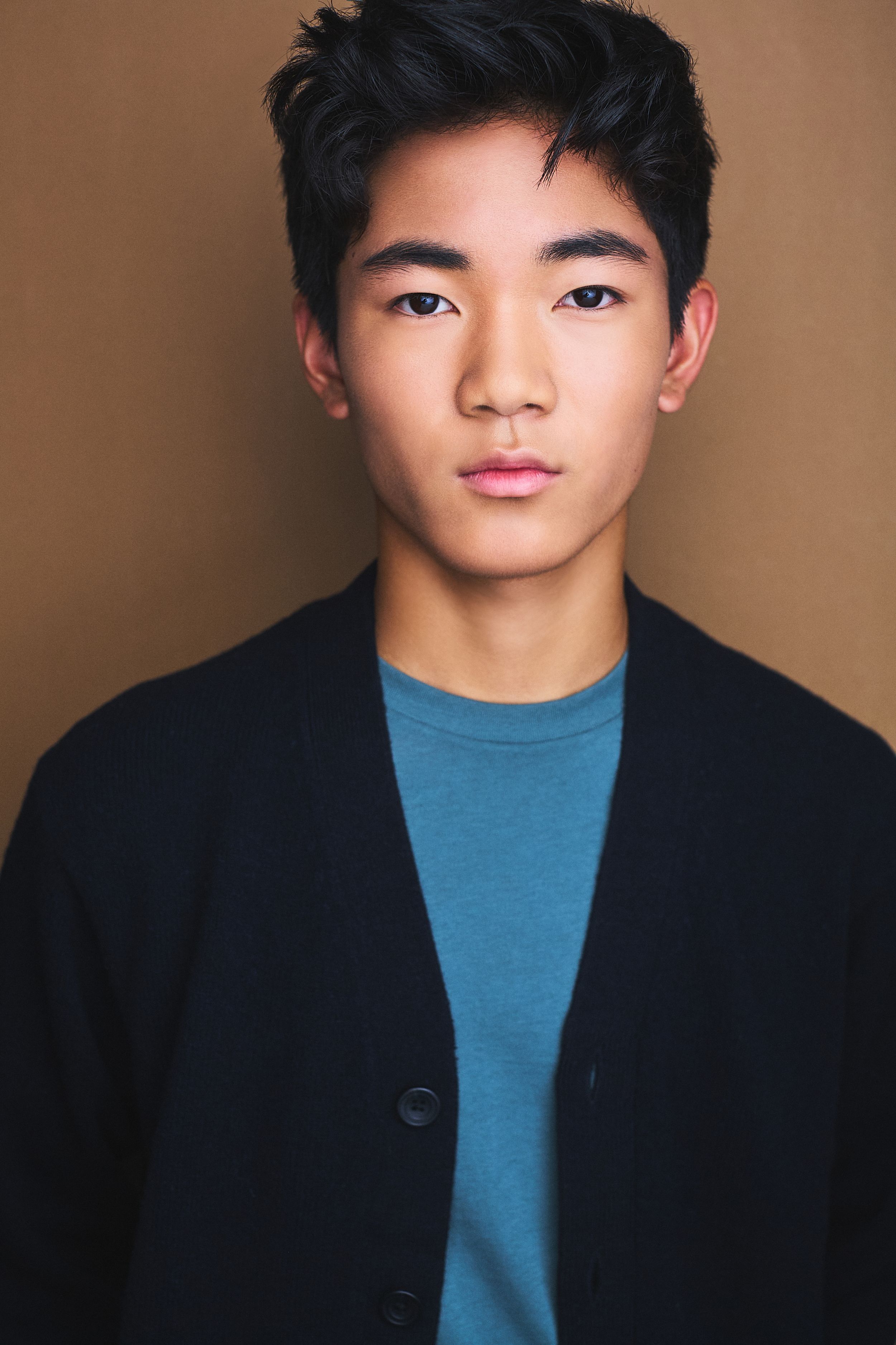 Headshot of a young teenager in a blue shirt and blazer against a khaki background.
