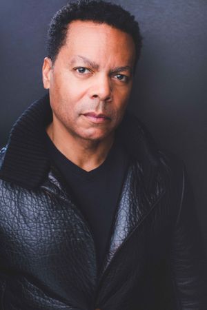 Headshot of a man in a black shirt and coat looking at the camera.