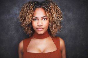 Headshots of a beautiful young woman with blonde curly hair in a brown cut out top against a dark background.