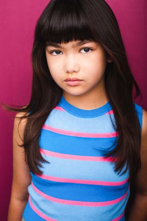 Headshot of girl with black hair and bangs in a blue and pink striped tank top.