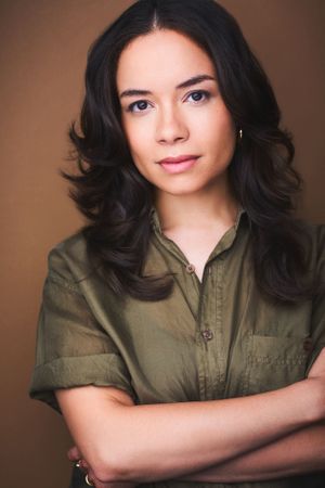 Headshot of University of Michigan actor Sydney Morton in in a green shirt with arms crossed against a tan background.