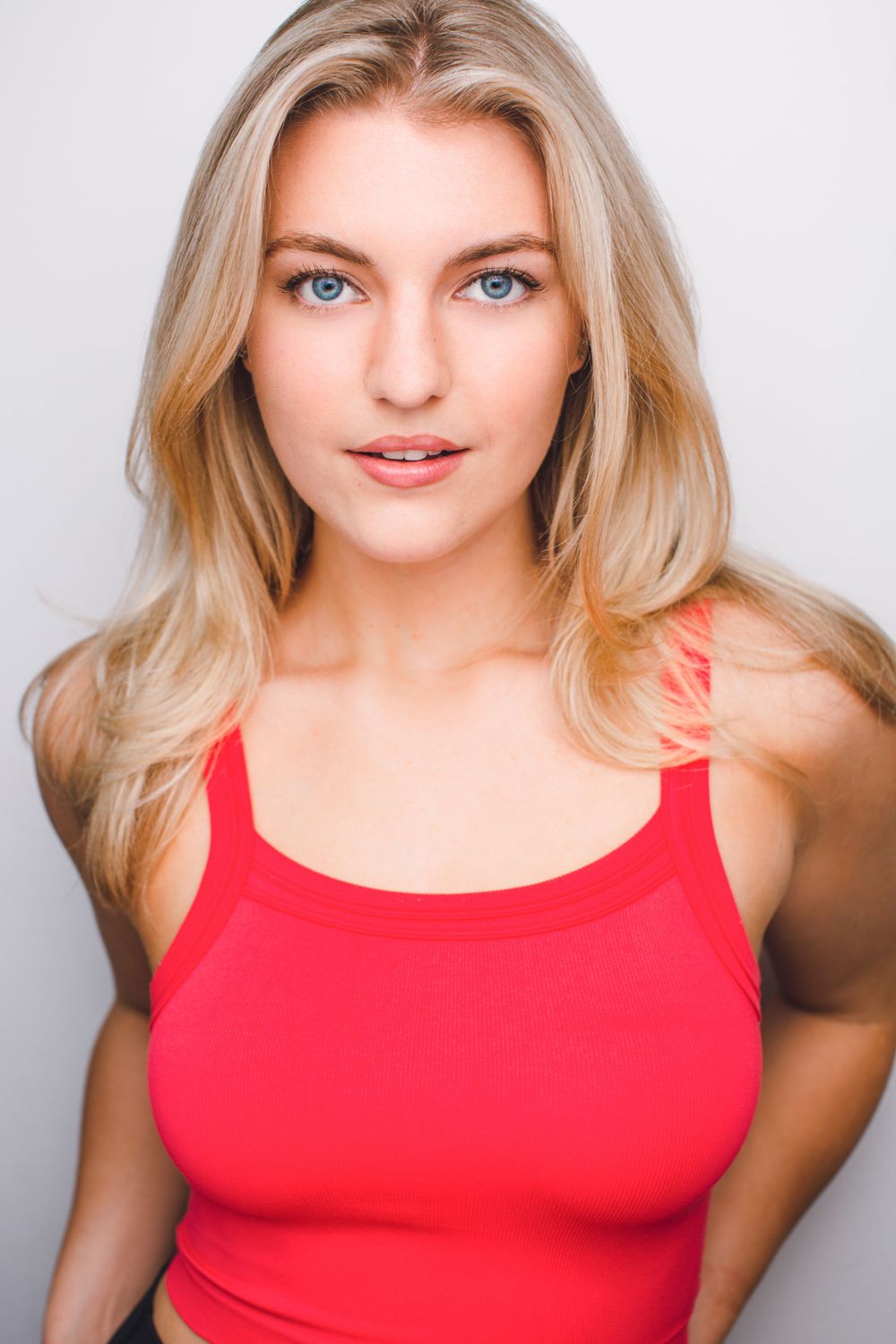 Headshot of a beautiful blonde woman in a red tank top against a white background.