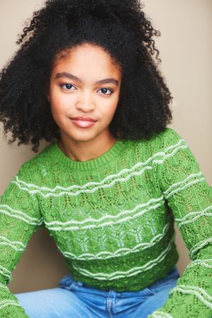 Headshot of a young teenage girl in a green sweater against a tan background.