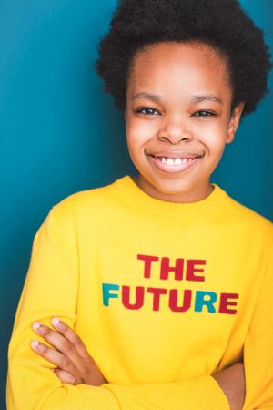 Headshot of a young boy in a bright yellow sweater that reads "The Future" with arms crossed against a blue background.