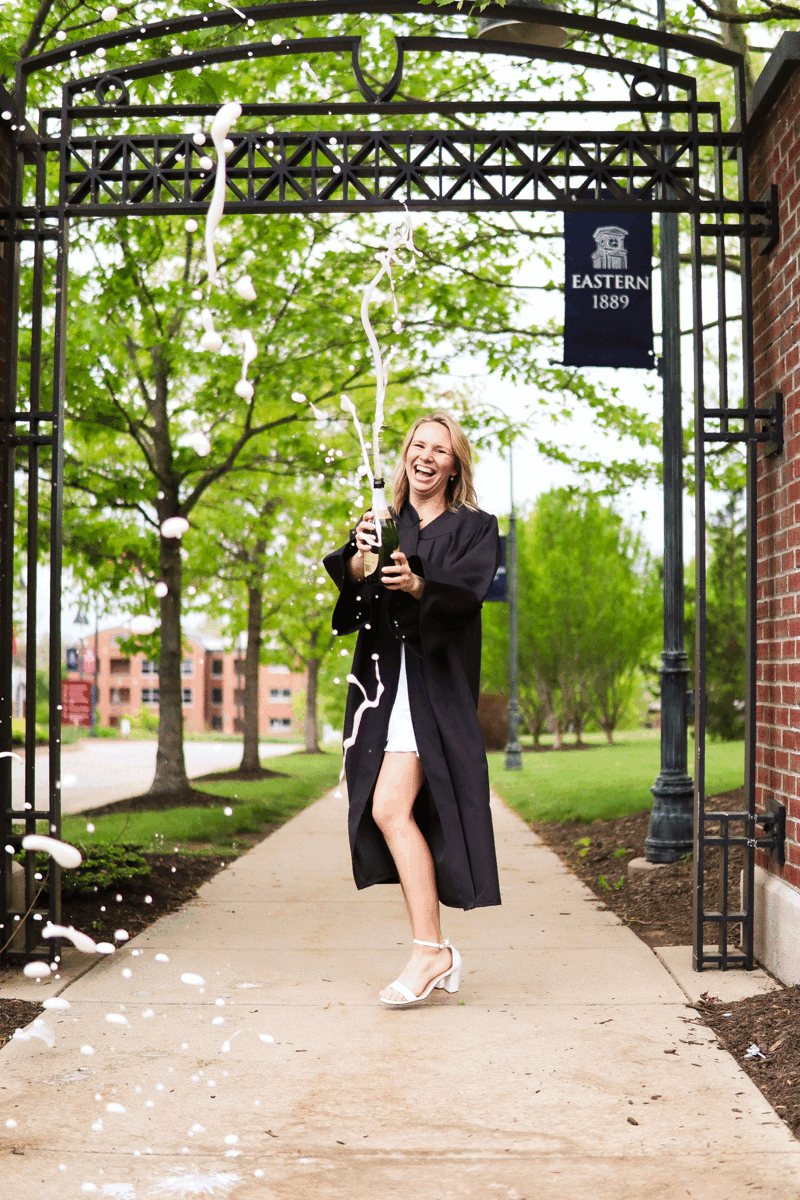 Gif of a female graduate popping and spraying champagne.