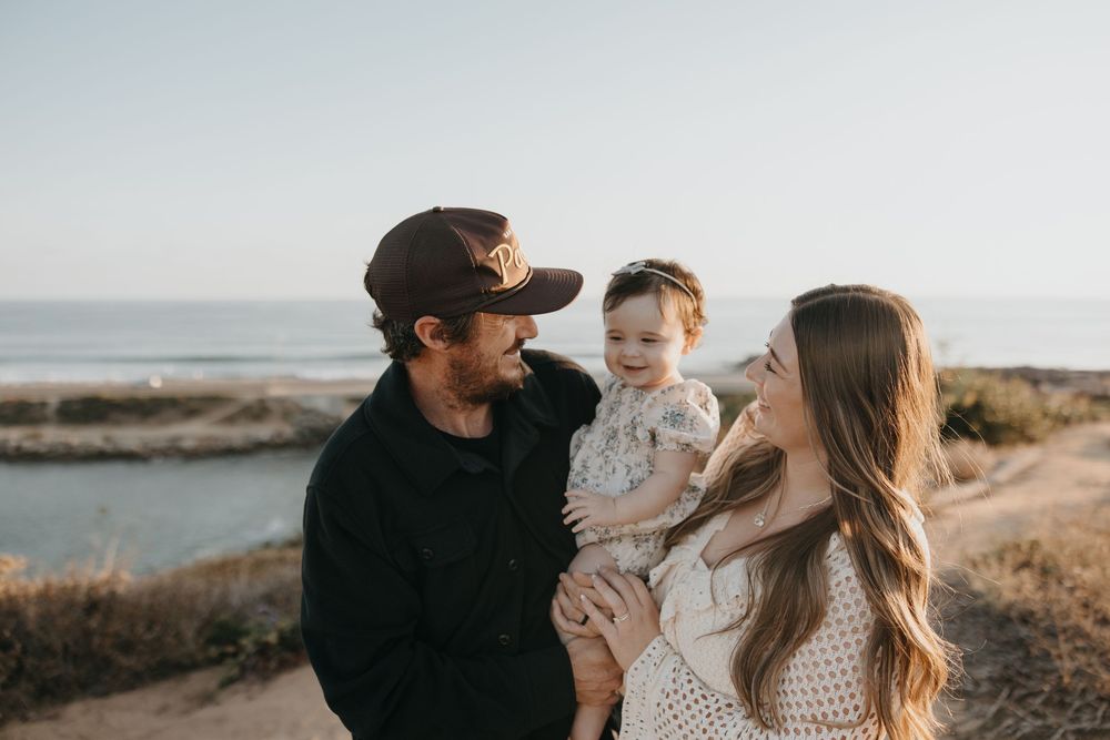 A family shares an intimate moment together on a coastal cliff overlooking the ocean during golden hour.
