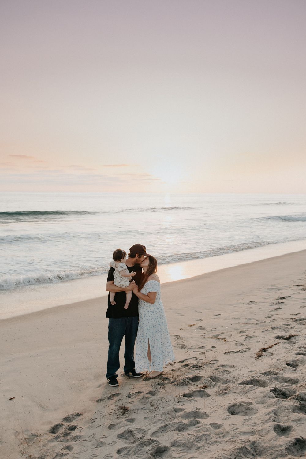Couple shares romantic moments on a sandy beach at sunset with gentle ocean waves in the background.