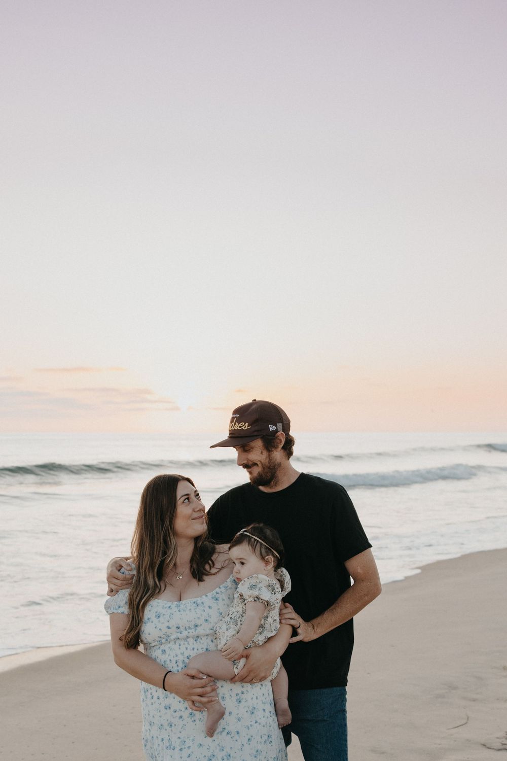 A family enjoys a tender moment together on the beach at sunset with waves rolling in the background.
