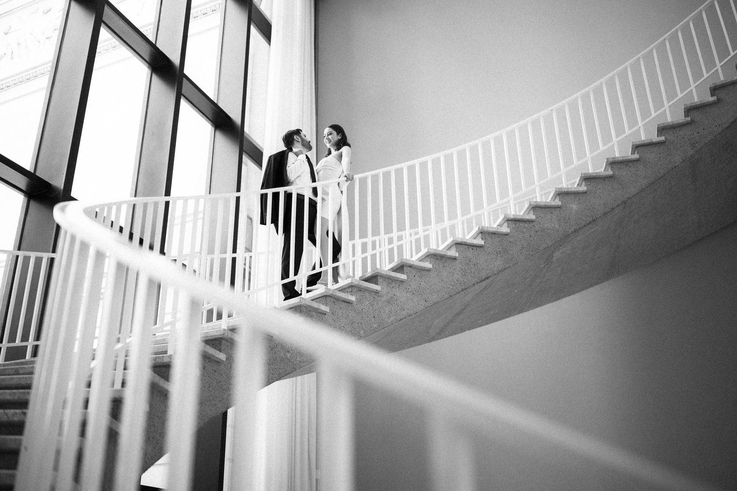 A couple stands together on a minimalist white staircase in a black and white composition.