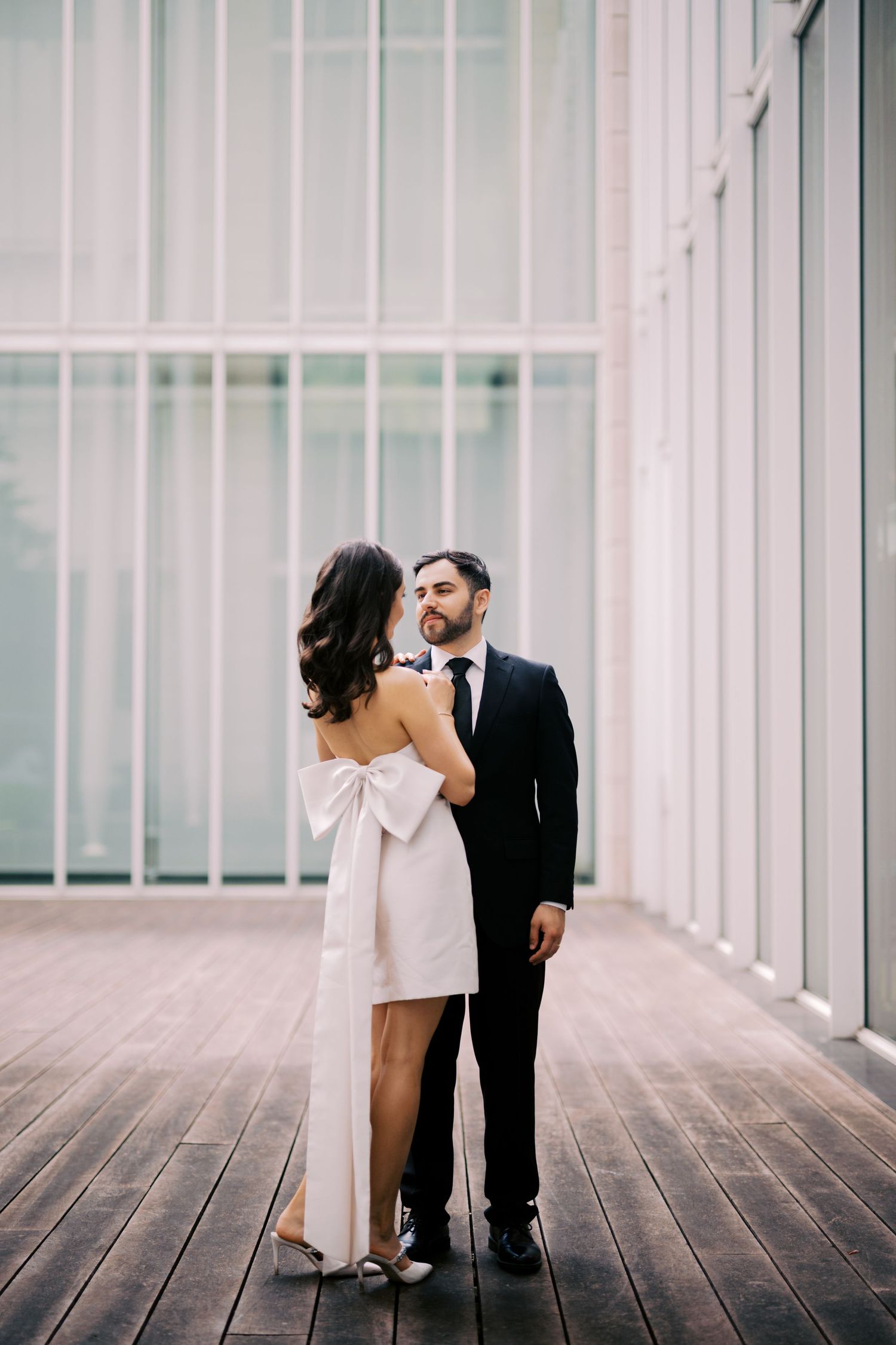 A couple in formal attire pose together against a modern white architectural backdrop.