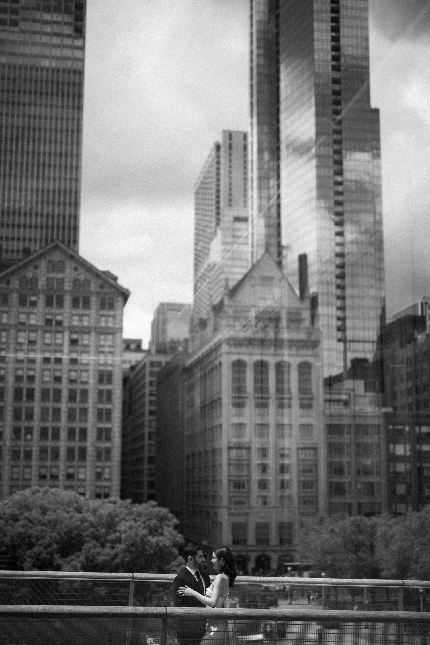 A black and white cityscape photo featuring a couple with towering skyscrapers behind them.