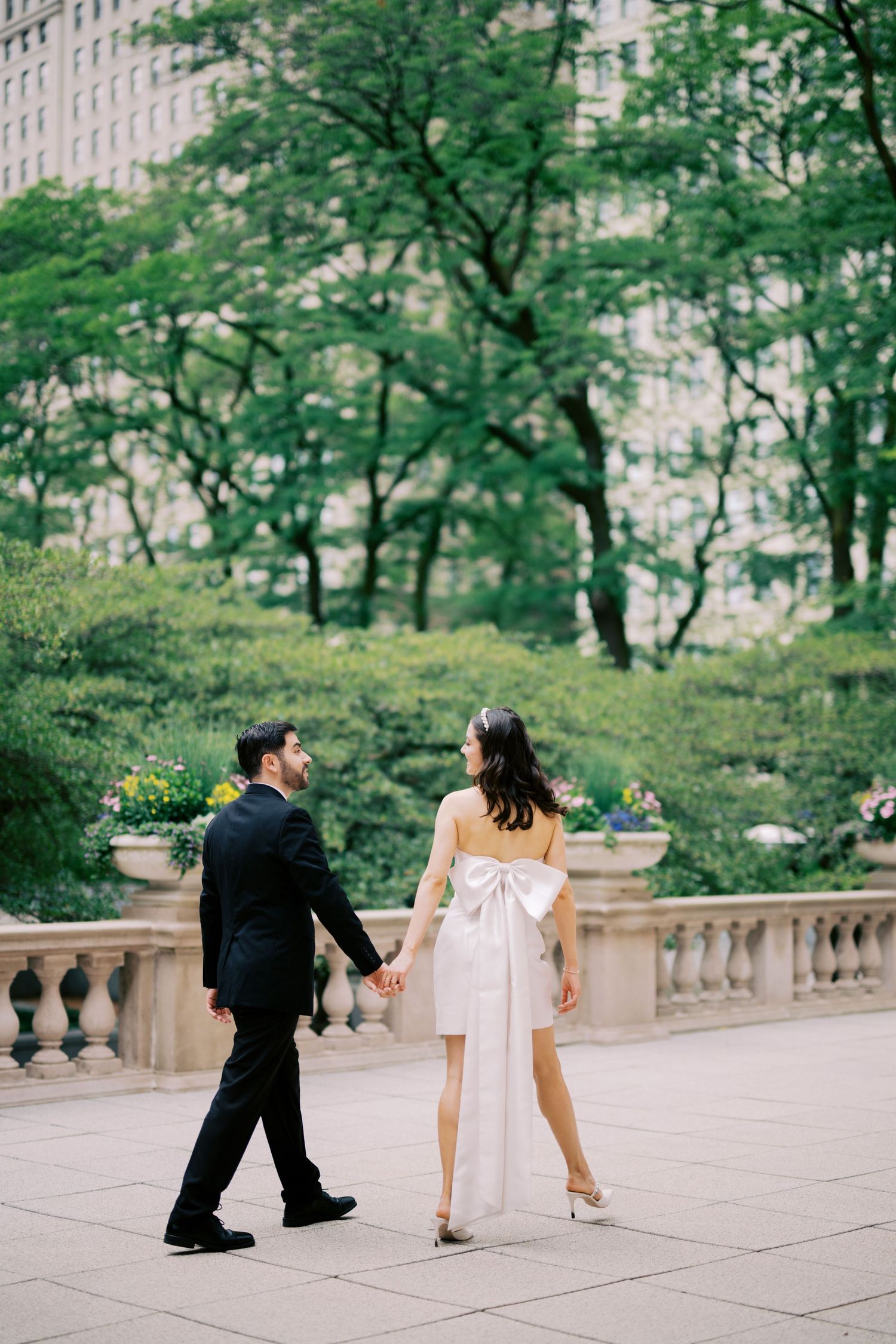 Couple walking along an elegant stone terrace with city buildings in the background.