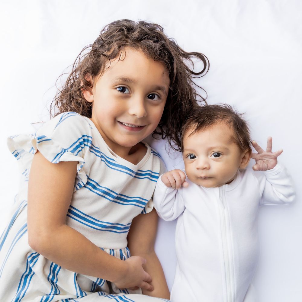Young girl in striped dress smiling while holding newborn baby sibling on white background in Connell, Wa.