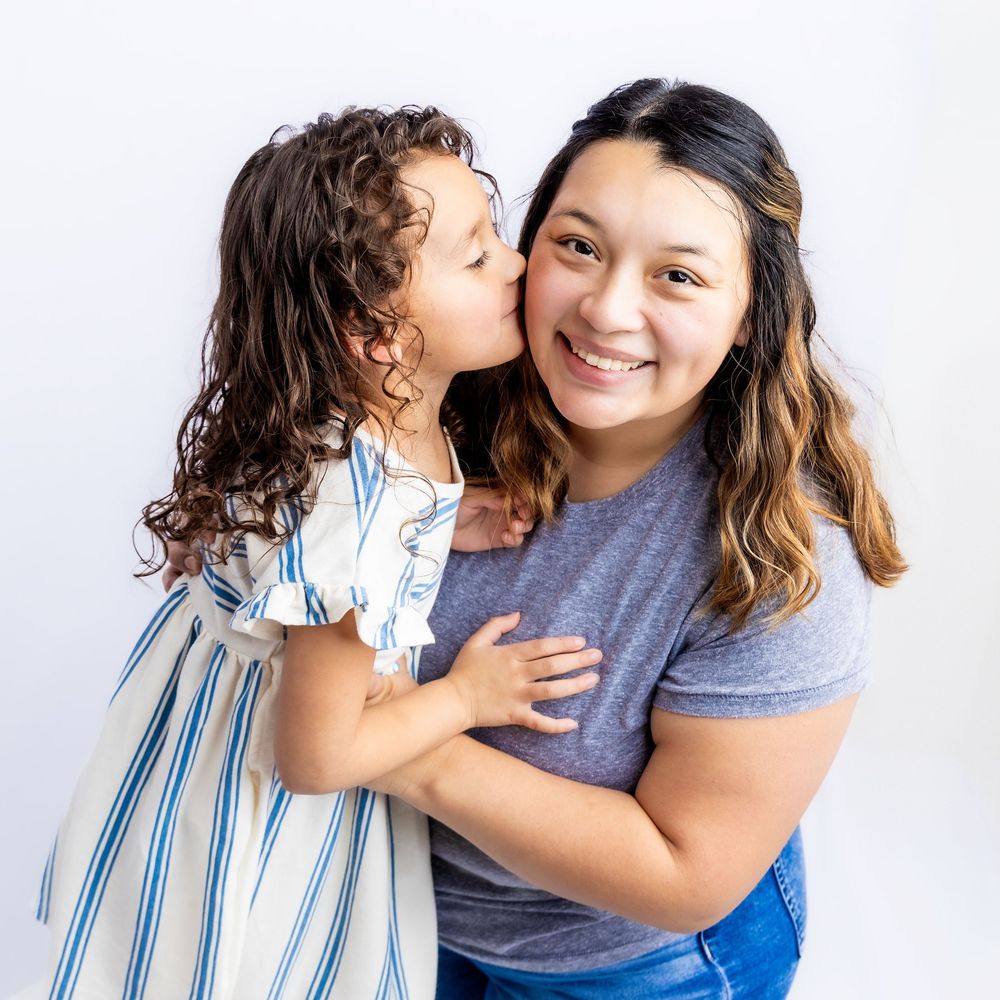 Little girl with curly hair kissing her smiling mother on the cheek in a studio portrait in Connell, Wa.