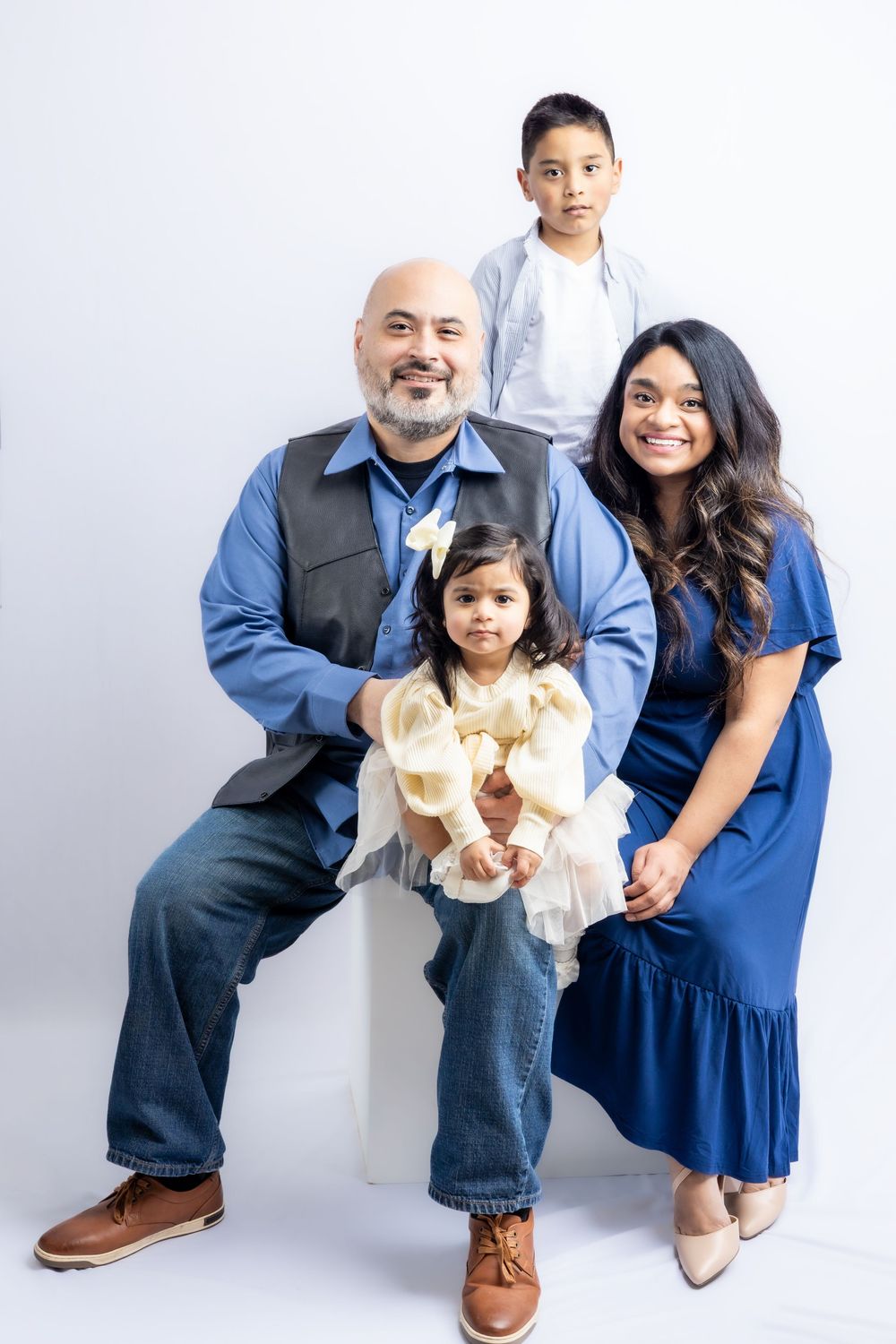 Family of four posing for a studio portrait, parents in blue outfits with two young children in Connell, Wa.