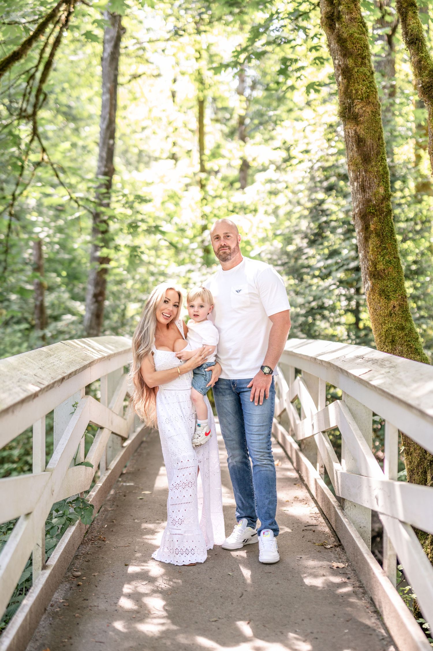 A family stands together on a wooden footbridge in a lush green forest on a sunny summer day.