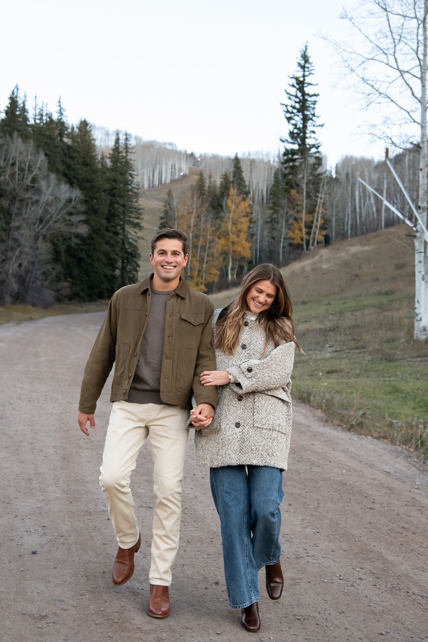 A stylish fall couple want together in a cute candid pose with the mountains and trees around them on a dirt road in Vail Colorado
