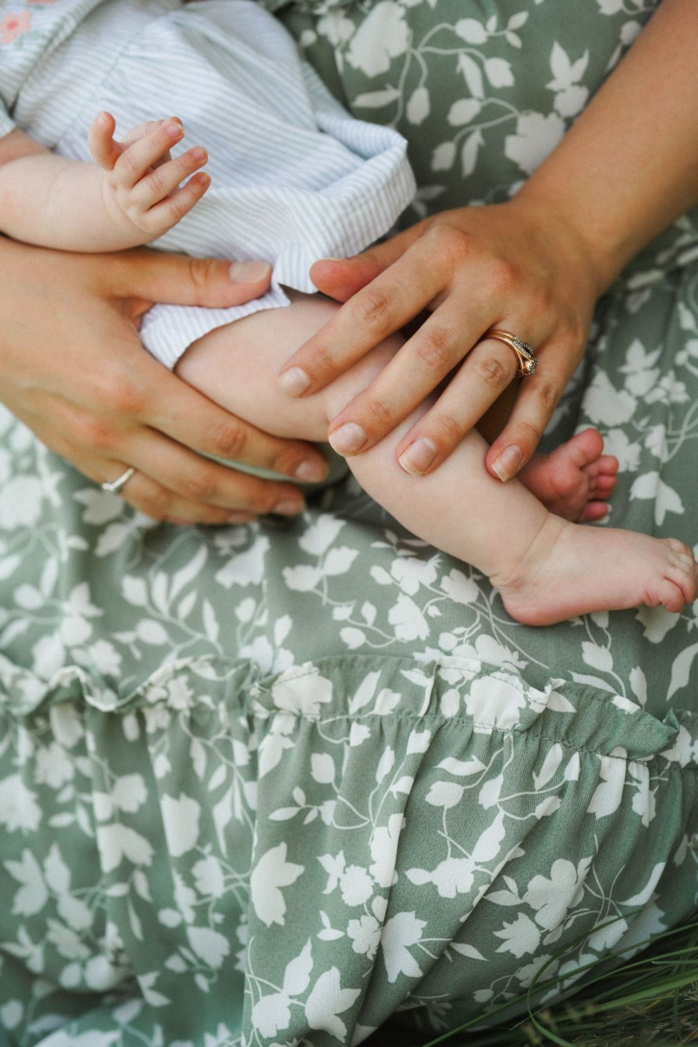 Hands gently massage a baby's tiny feet against a green and white floral patterned background.