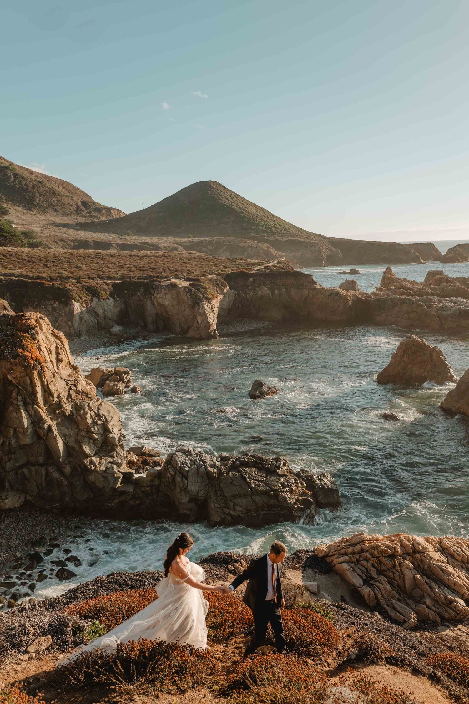 bride and groom walking down the cliffs in big sur