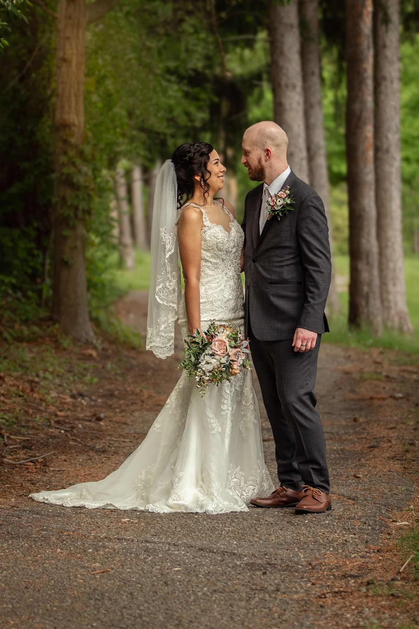 Wedding guests gather around a white floral-decorated outdoor ceremony space with trees in the background.