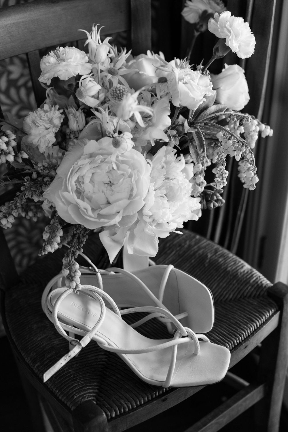 Elegant white bridal bouquet with peonies next to strappy wedding shoes in black and white.