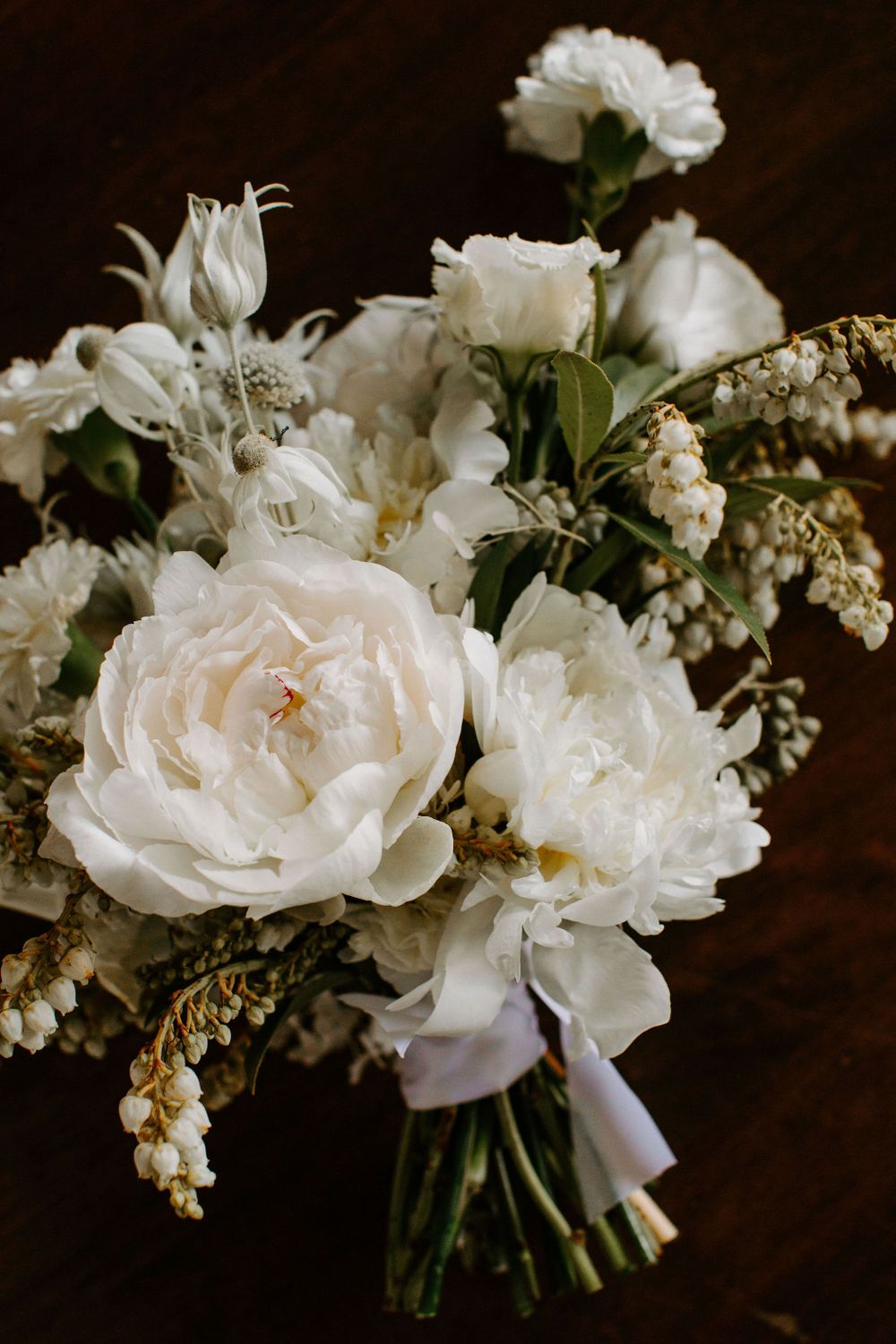 Romantic white wedding bouquet featuring peonies and delicate greenery tied with ribbon.