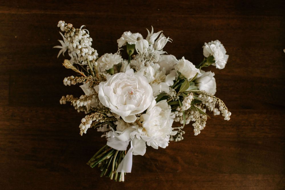 Overhead view of white wedding bouquet with roses and baby's breath on dark wooden surface.