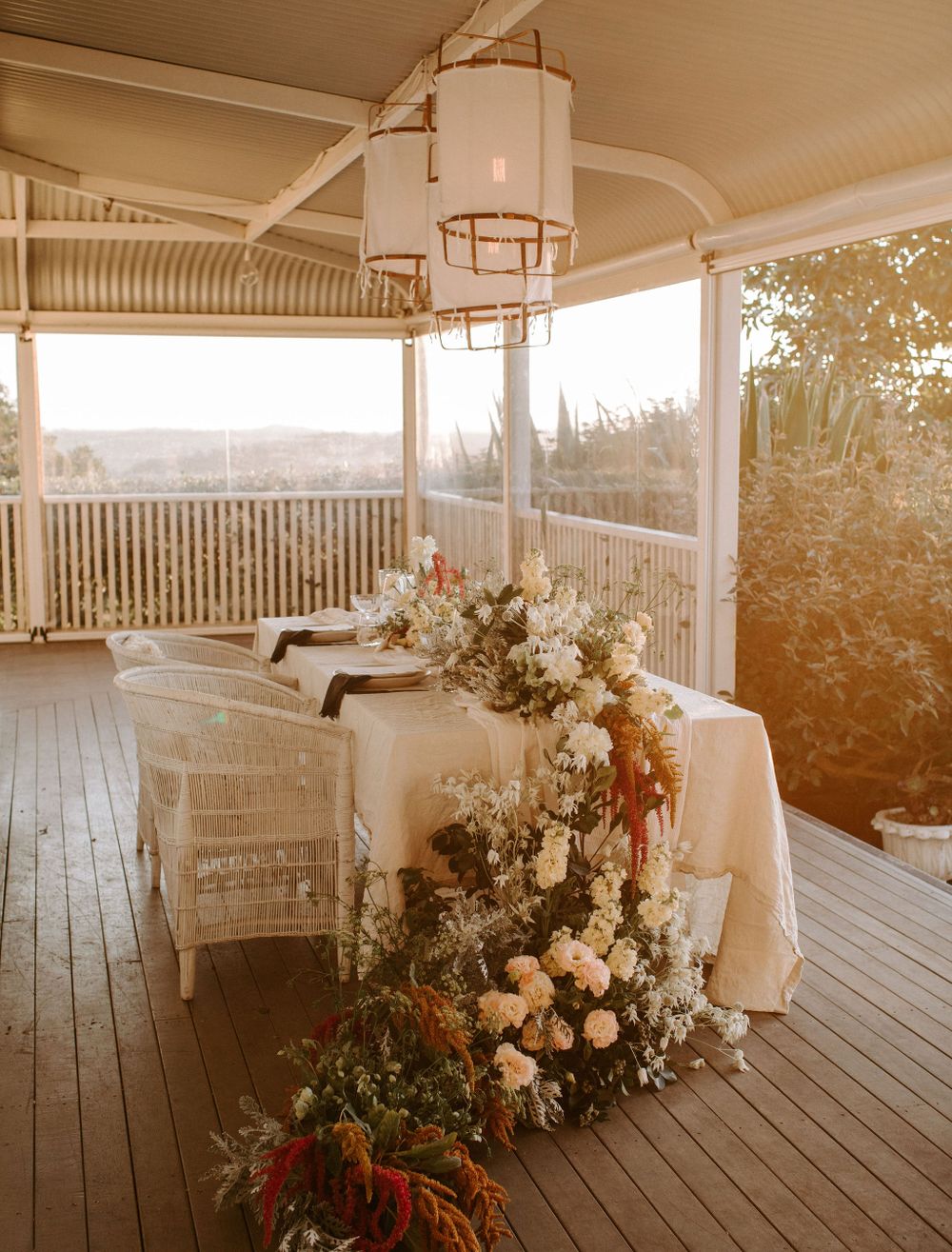 Romantic wedding table setup on veranda with floral arrangements and hanging lantern.