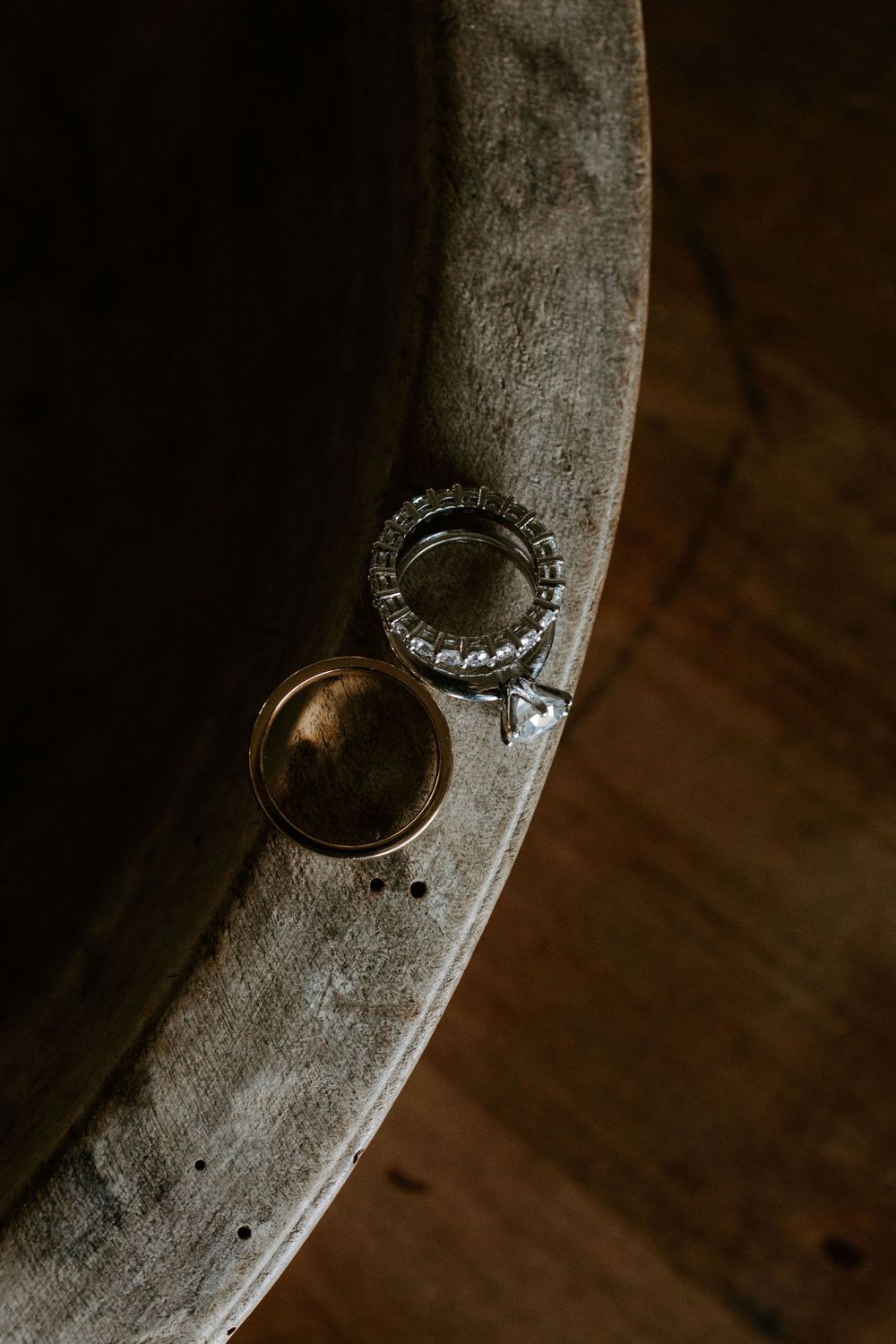 Two wedding rings displayed on a rustic wooden surface in dramatic lighting.