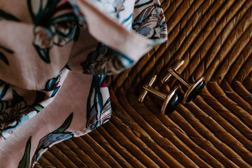 Silver cufflinks on wooden surface next to floral patterned fabric.