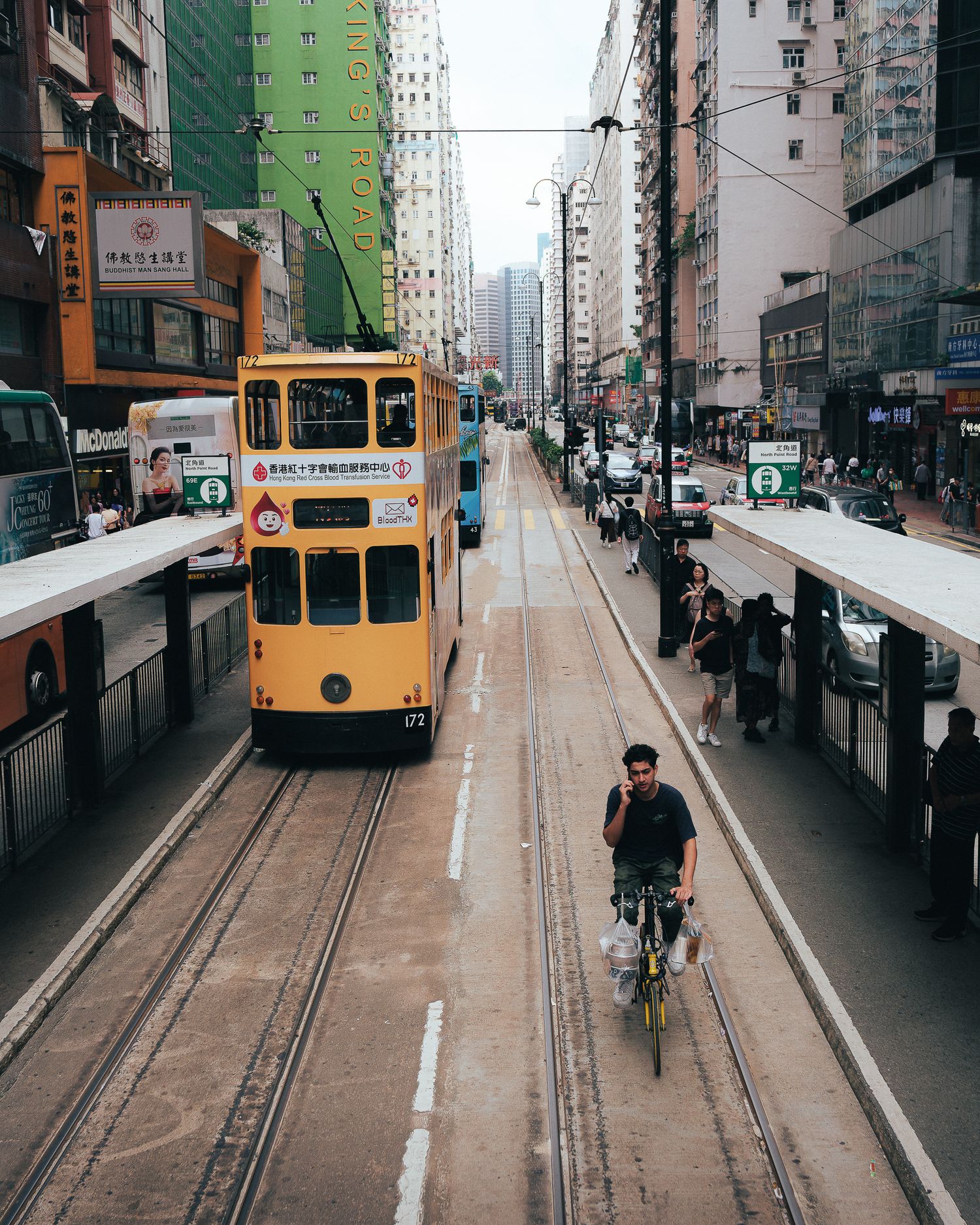 A vintage yellow tram travels down a busy Hong Kong street lined with tall buildings.