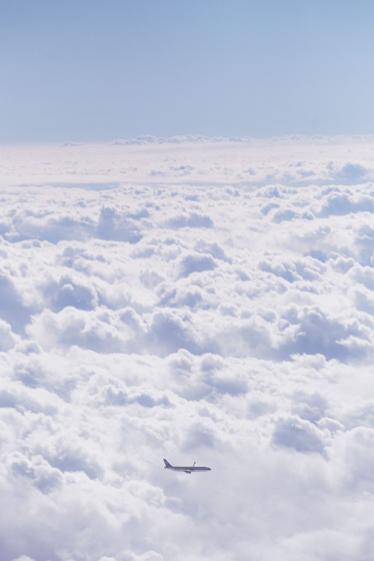 Small airplane flying below a sea of fluffy white clouds against pale blue sky.
