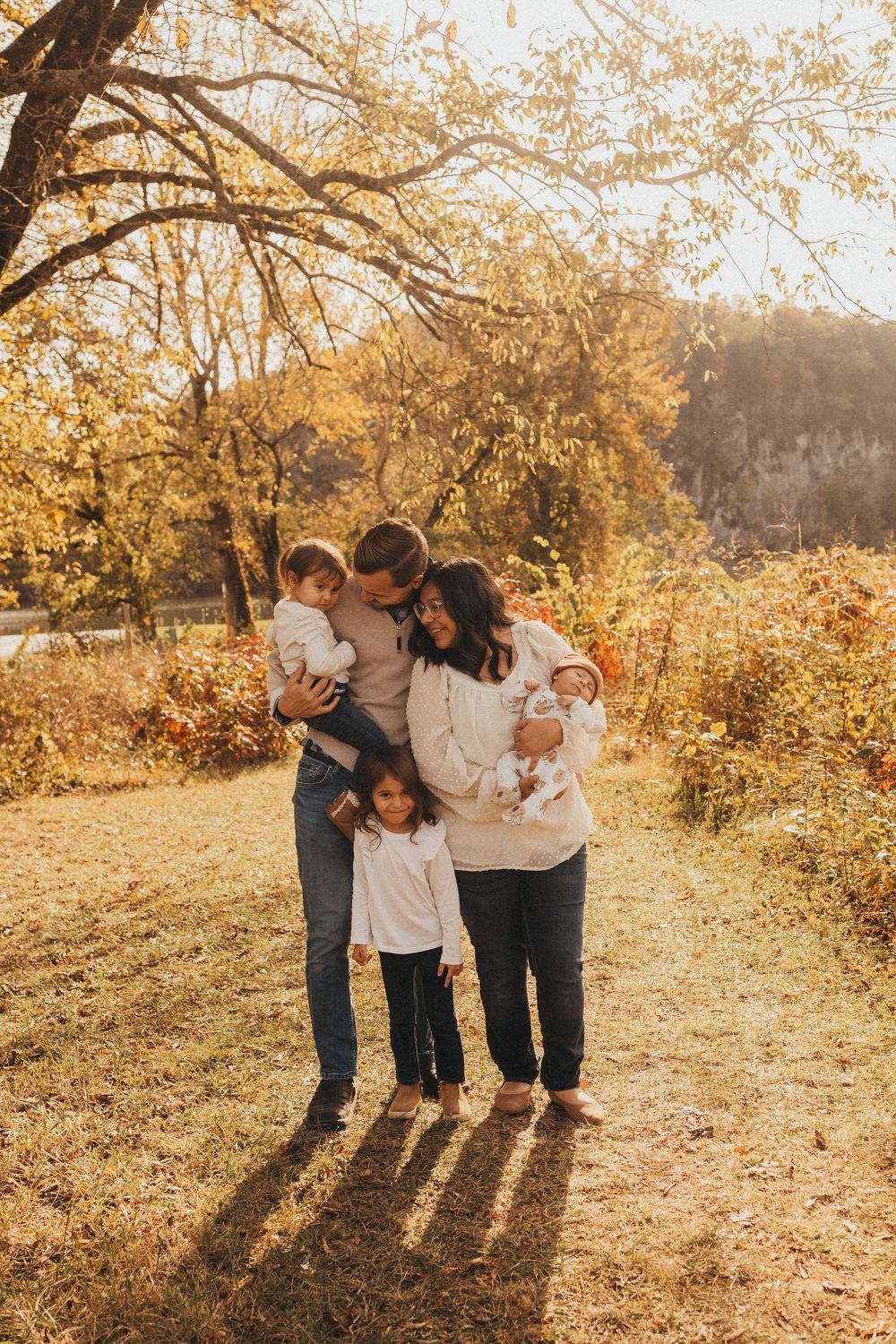 Family of four embraces warmly on a golden autumn path surrounded by colorful fall foliage.