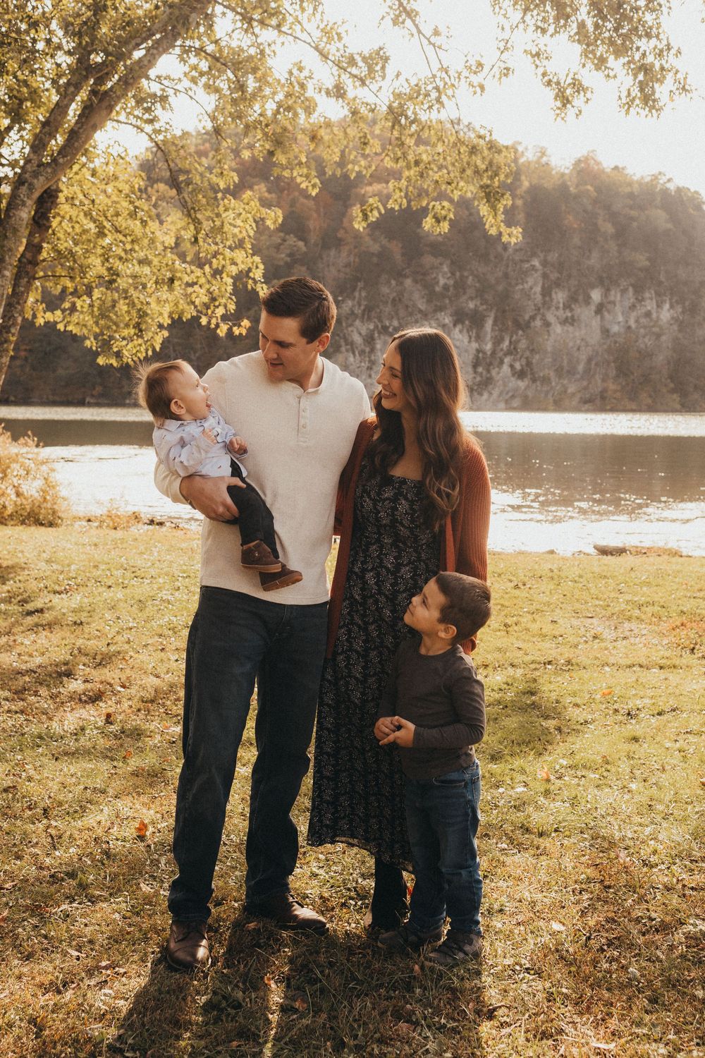 Young family of four shares a warm moment by a sunlit river during fall season.