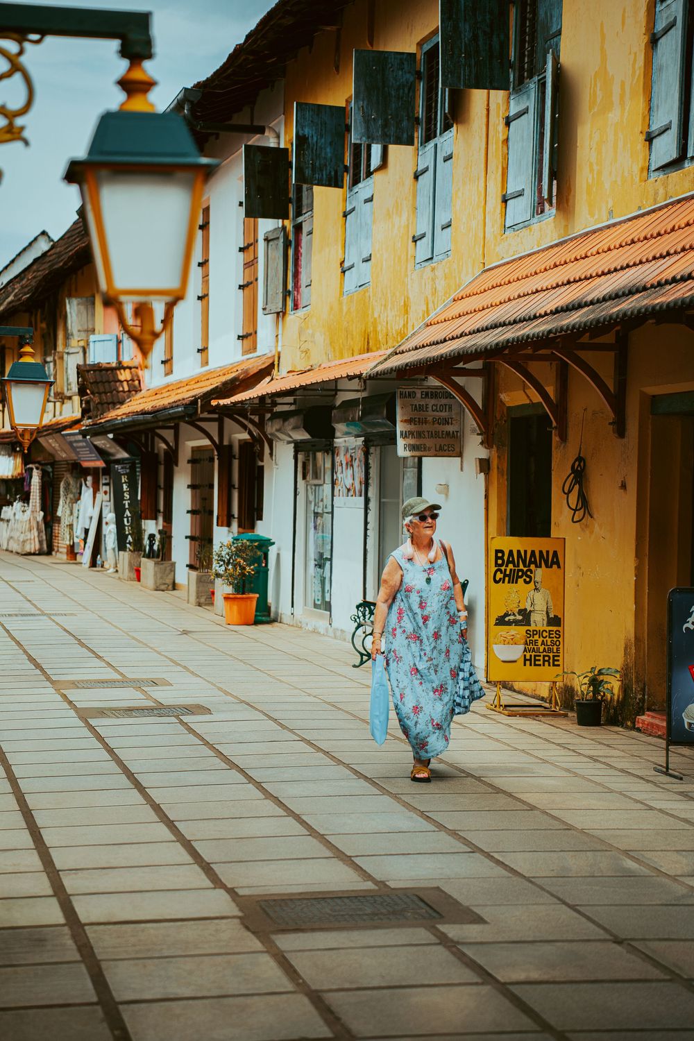 A person in a blue dress walks along a colonial-style street with yellow walls and wooden shutters in Galle Fort, Sri Lanka.