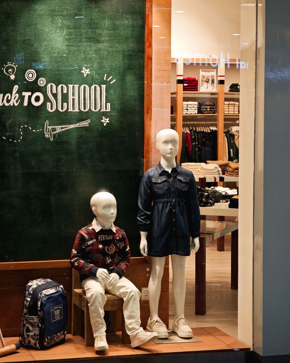 Back to school retail display with backpacks and mannequins showcasing student fashion against a chalkboard backdrop.