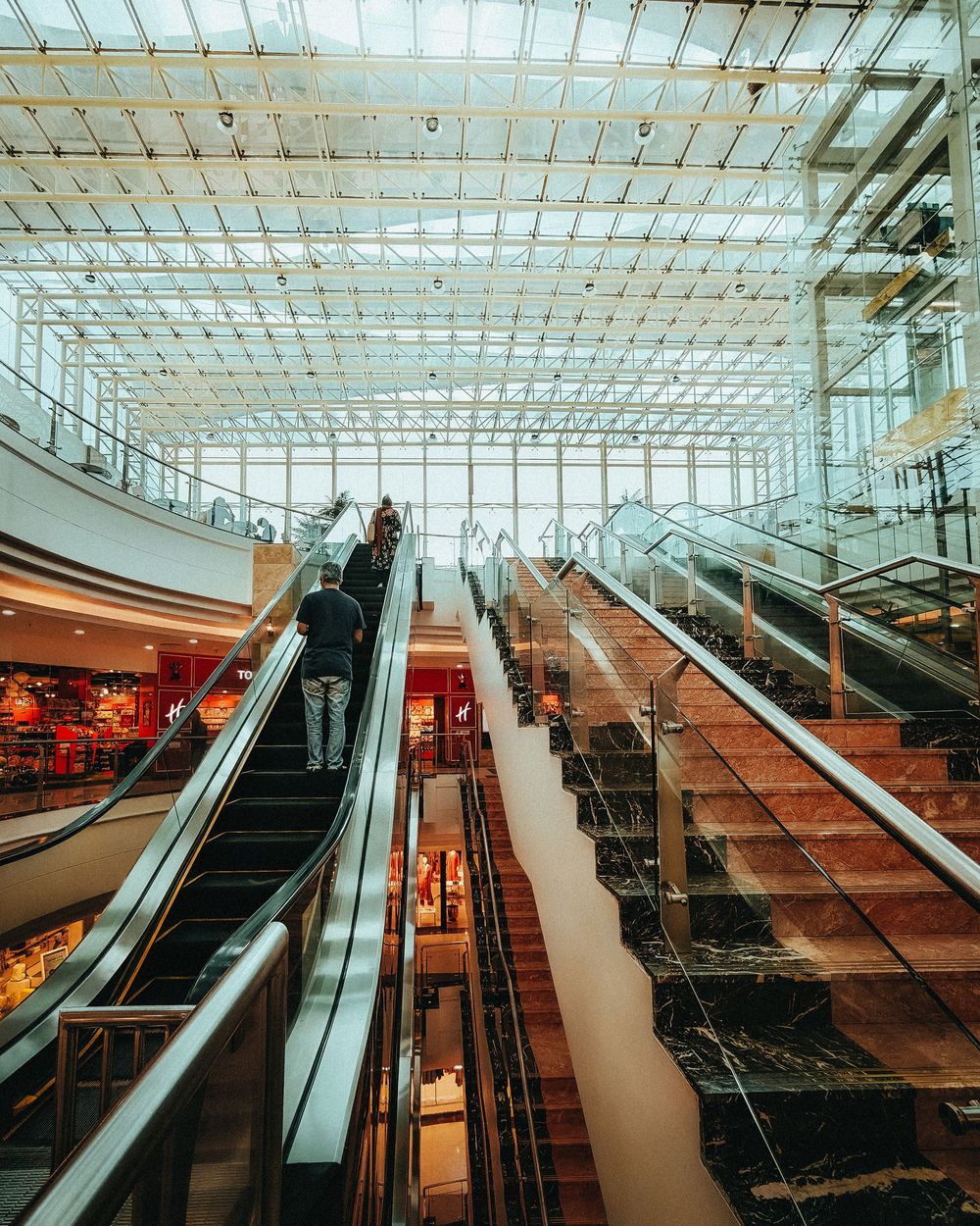 A sequence of modern escalators in a shopping mall with glass ceiling and natural lighting creating geometric patterns.