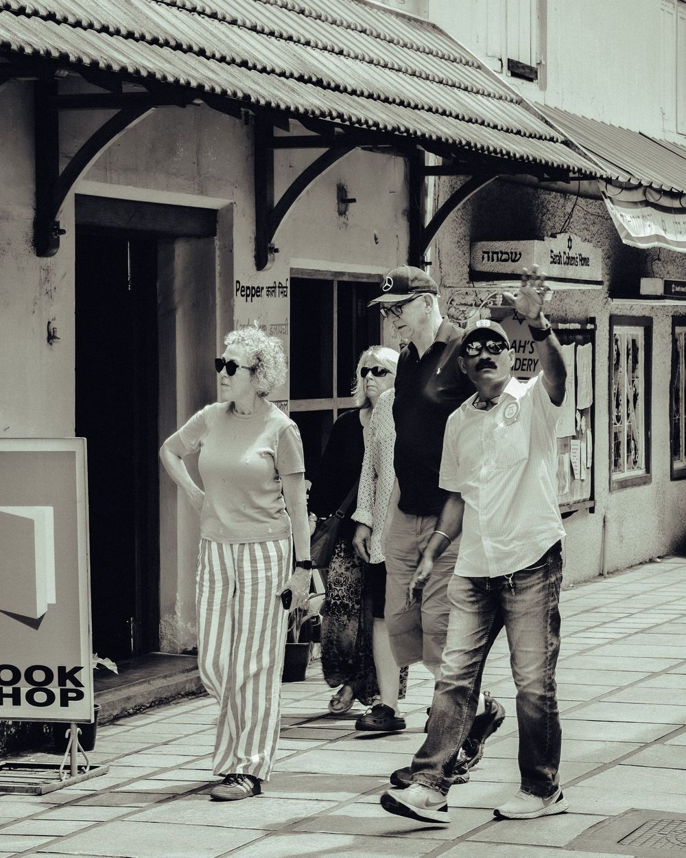 A sequence of black and white photos showing people walking along a covered sidewalk with storefronts.